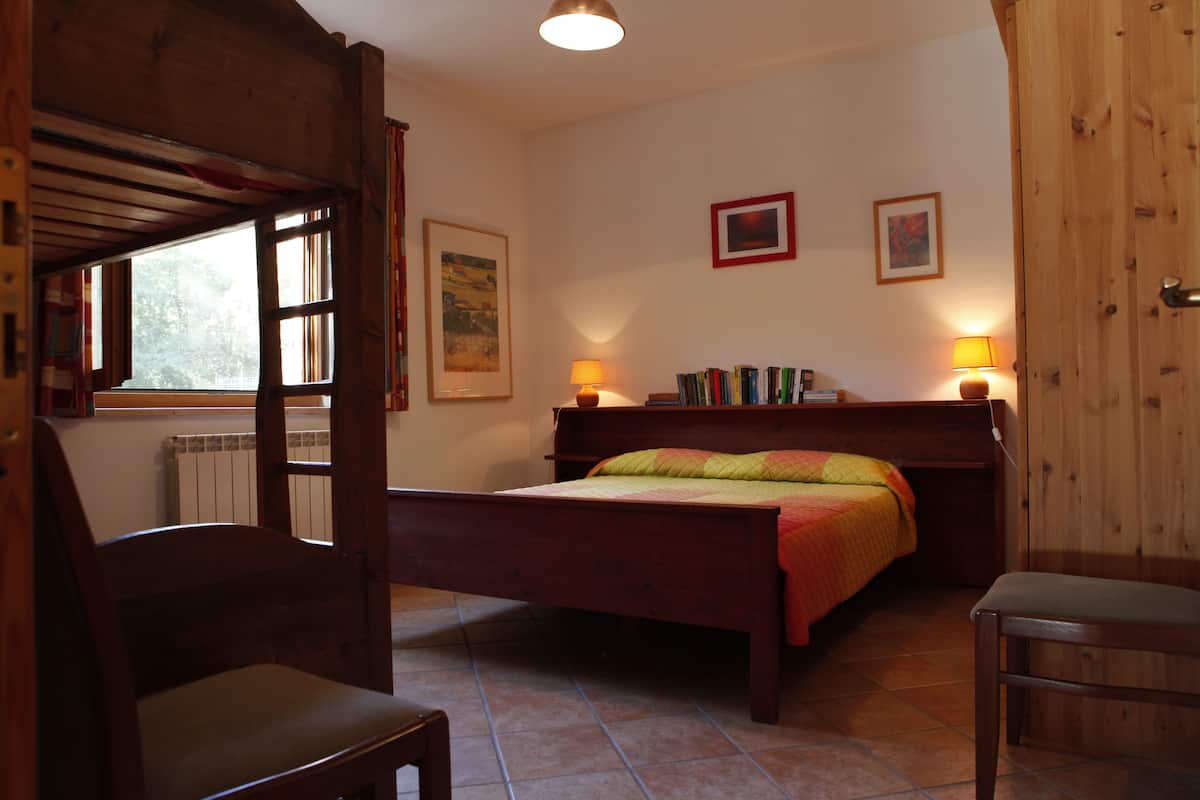 A bedroom with a wooden bed, two bedside lamps, a window with curtains, and a radiator.