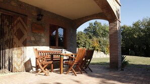 An outdoor patio with a stone wall, wooden table and chairs, and a brick column. - Agriturismo Walden (Ficulle)