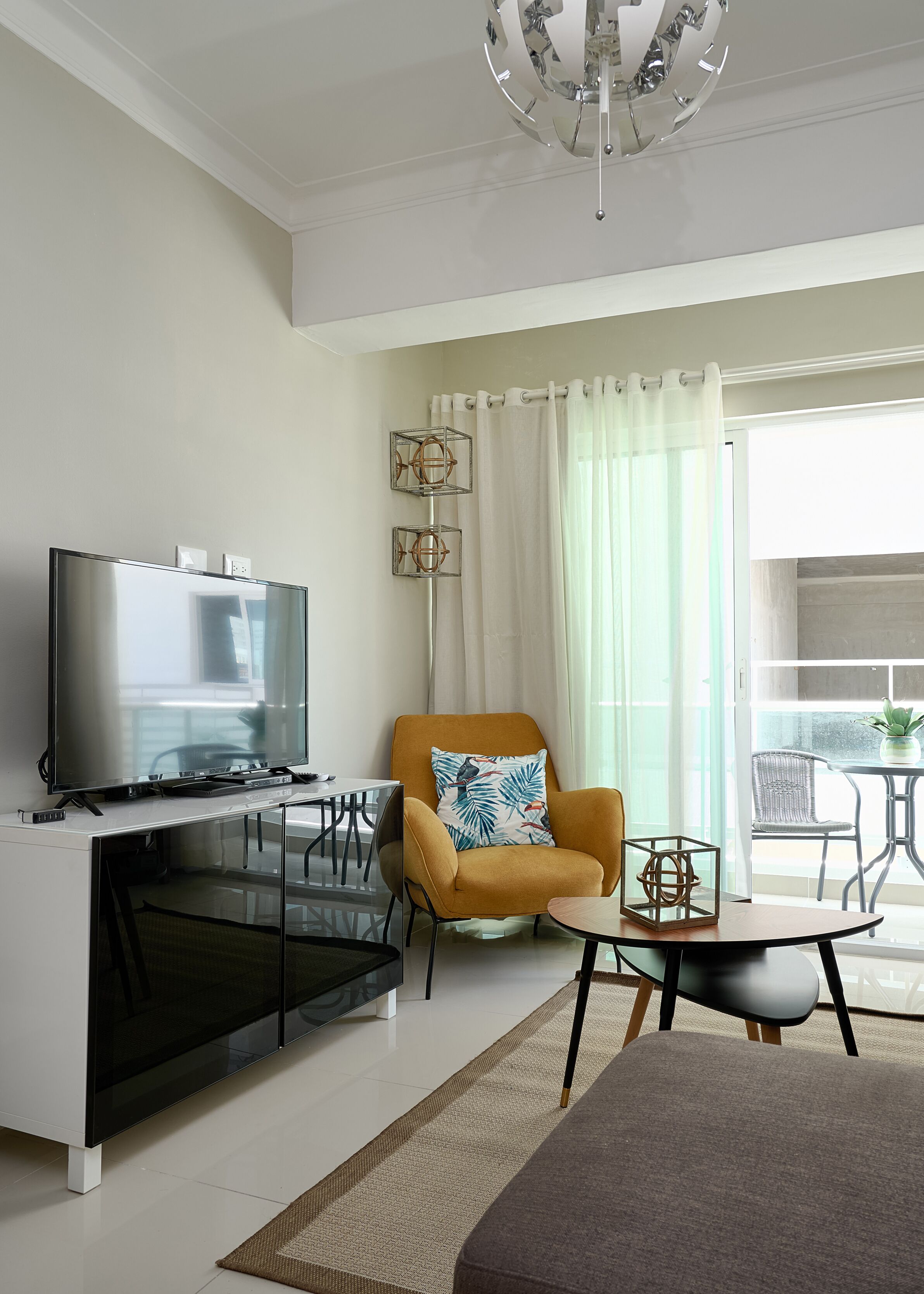 A modern living room with a flat-screen TV, a yellow armchair, a small round table, and a glass coffee table.