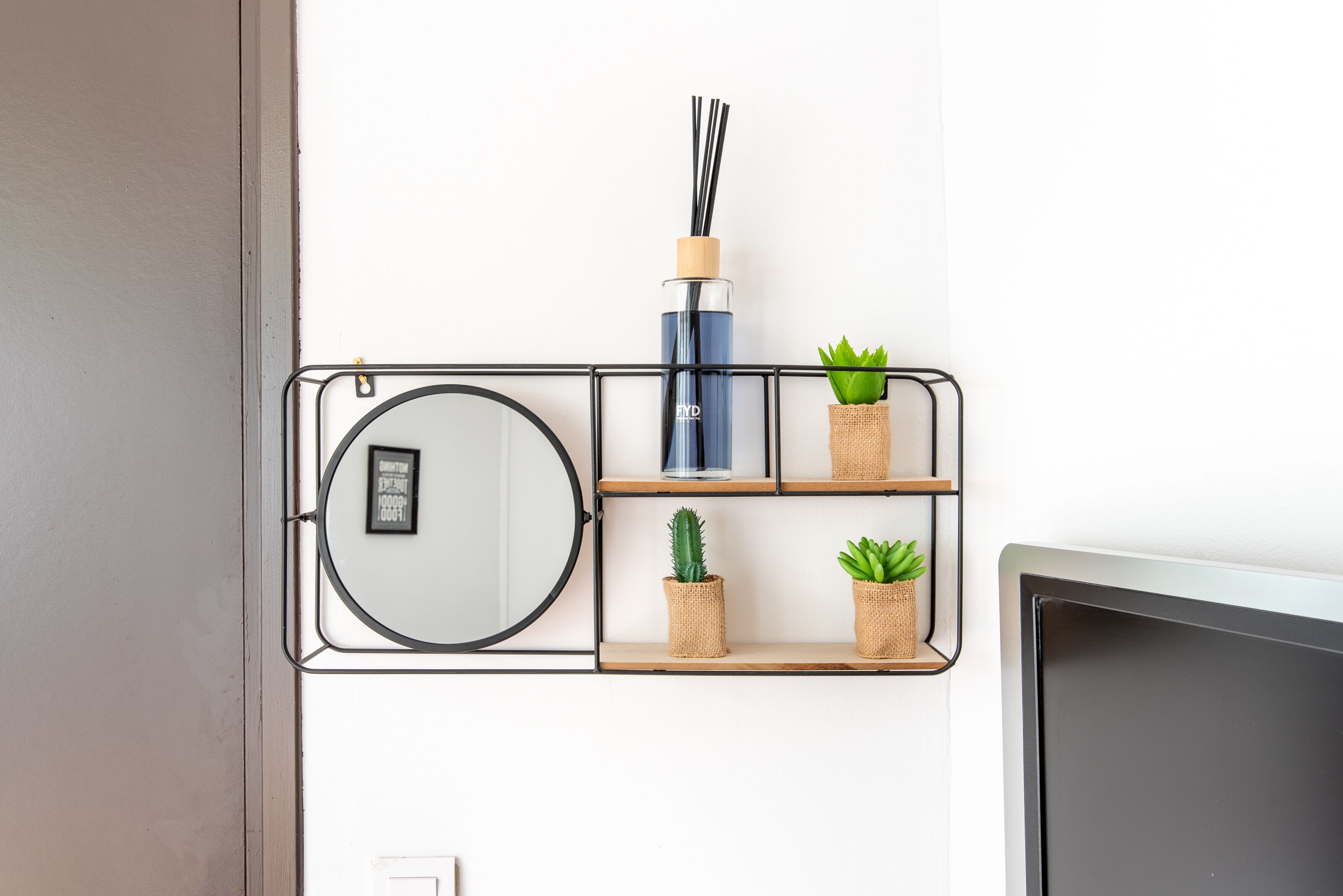 A wall-mounted shelf with a round mirror, a blue bottle, and three small potted plants.