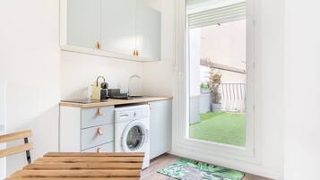 A compact kitchen with a washing machine, a sink, and a window overlooking a garden.