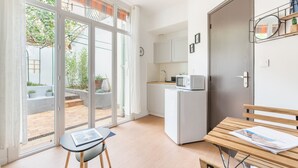Cocina compacta con microondas, lavaplatos y refrigerador. Hay un banco de madera con una revista, y una mesa con una silla.