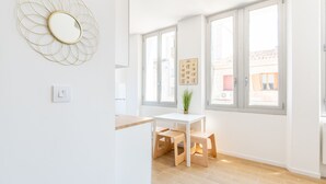 Una cocina moderna y luminosa, con encimera blanca, taburetes de madera y ventanas amplias con vistas a la ciudad.