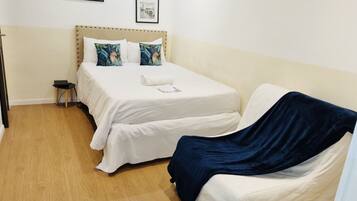 A bedroom with a bed, a bedside table, a chair, and two framed pictures on the wall.
