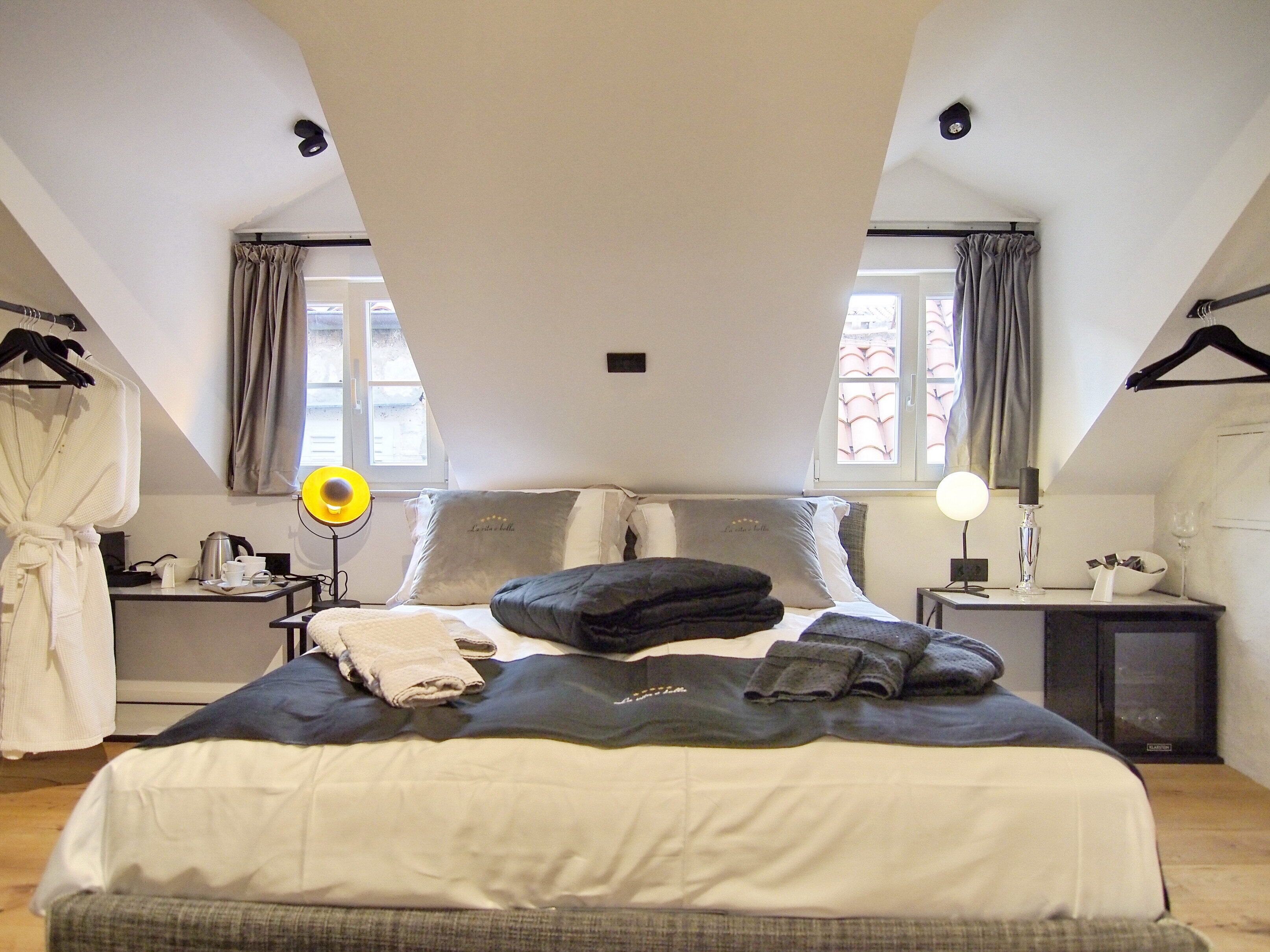 A bedroom with a large bed, two bedside tables, a wardrobe, and a window with curtains.