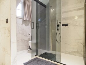 Ein modernes Badezimmer mit einer gläsernen Dusche, Marmorwänden und einer sichtbaren Toilette.