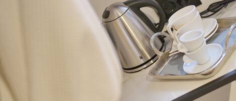 Una tetera de acero inoxidable y tazas blancas sobre una bandeja.