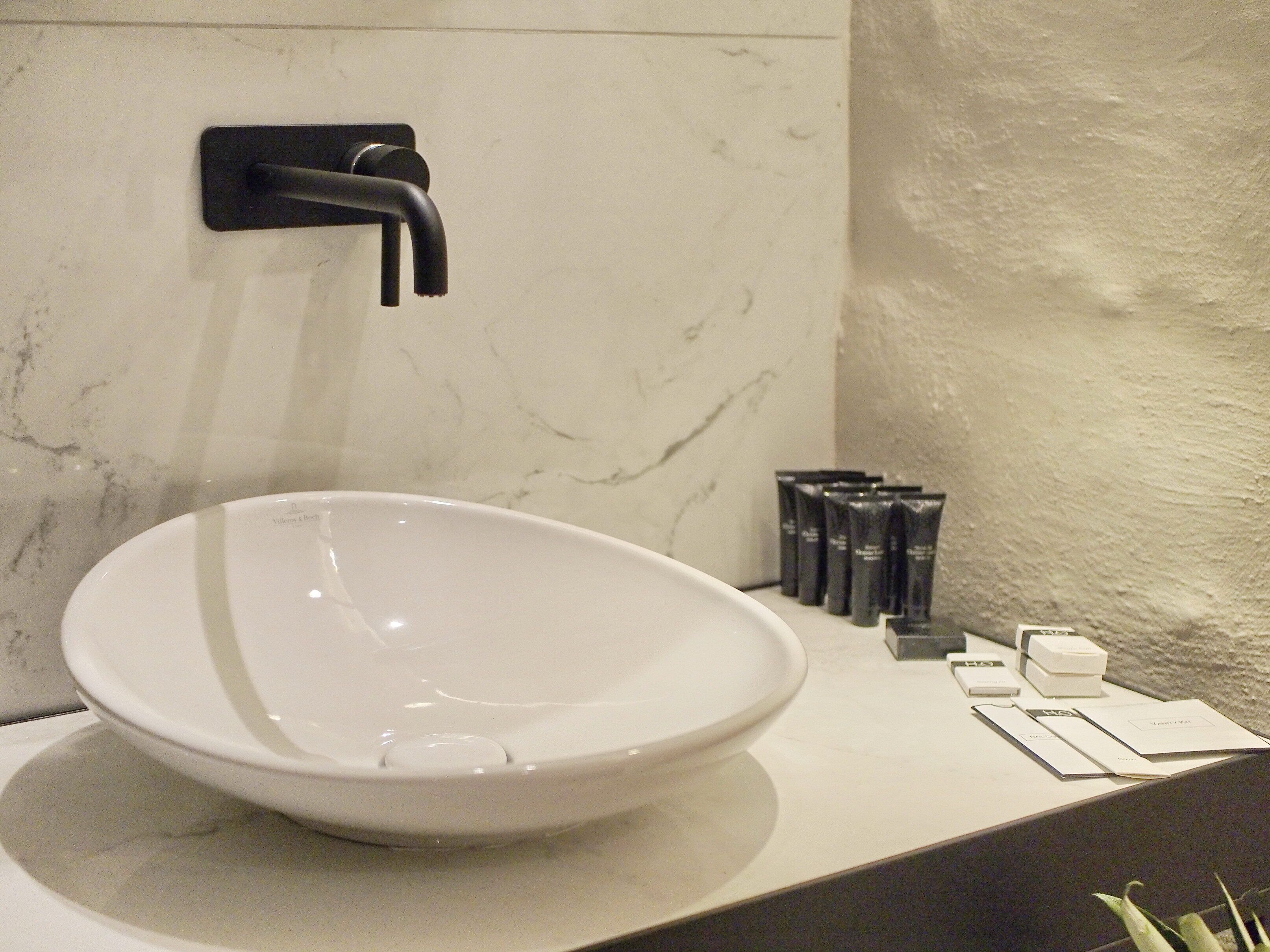 A white ceramic sink with a modern faucet, a marble backsplash, and toiletries on the counter.