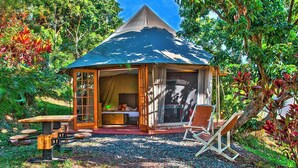 A small, open-air tent with a pitched roof, a wooden bench, a folding chair, and a table. - Gadiamb City- Glamping (Saint-Pierre)