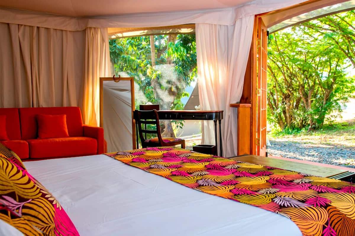 Habitación de hotel con una cama grande, un sofá rojo, un escritorio y vistas a zonas verdes.