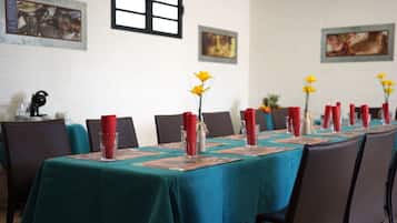 A conference room with a long table set for a meeting, featuring teal tablecloths, red napkins, and yellow flowers in vases.