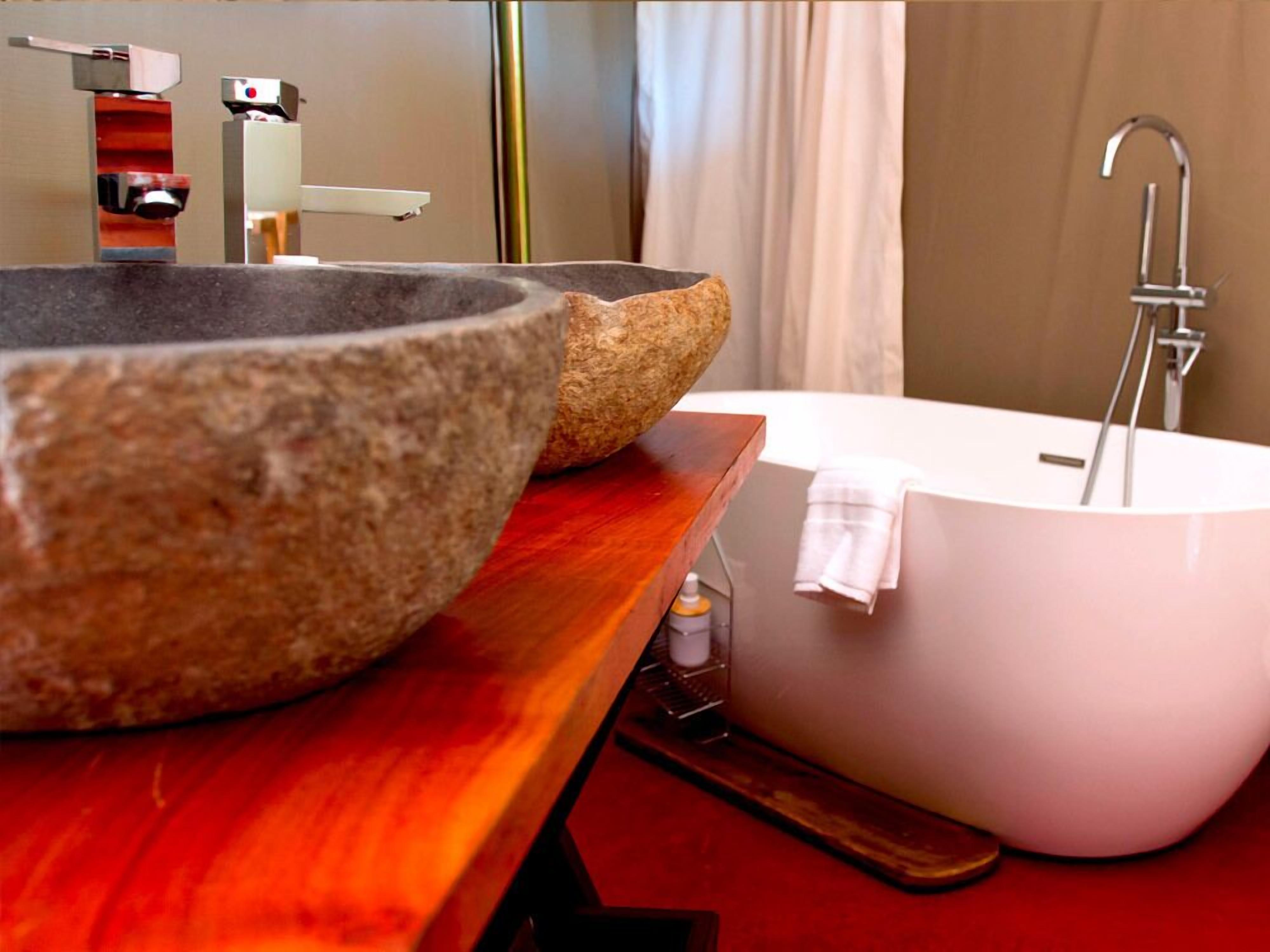 Une salle de bain avec un grand lavabo en pierre, une baignoire blanche et un meuble-lavabo en bois.