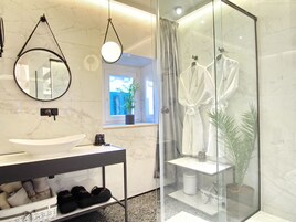 A modern bathroom with a large sink, a mirror, a glass shower enclosure, and a window with a view of the outside.