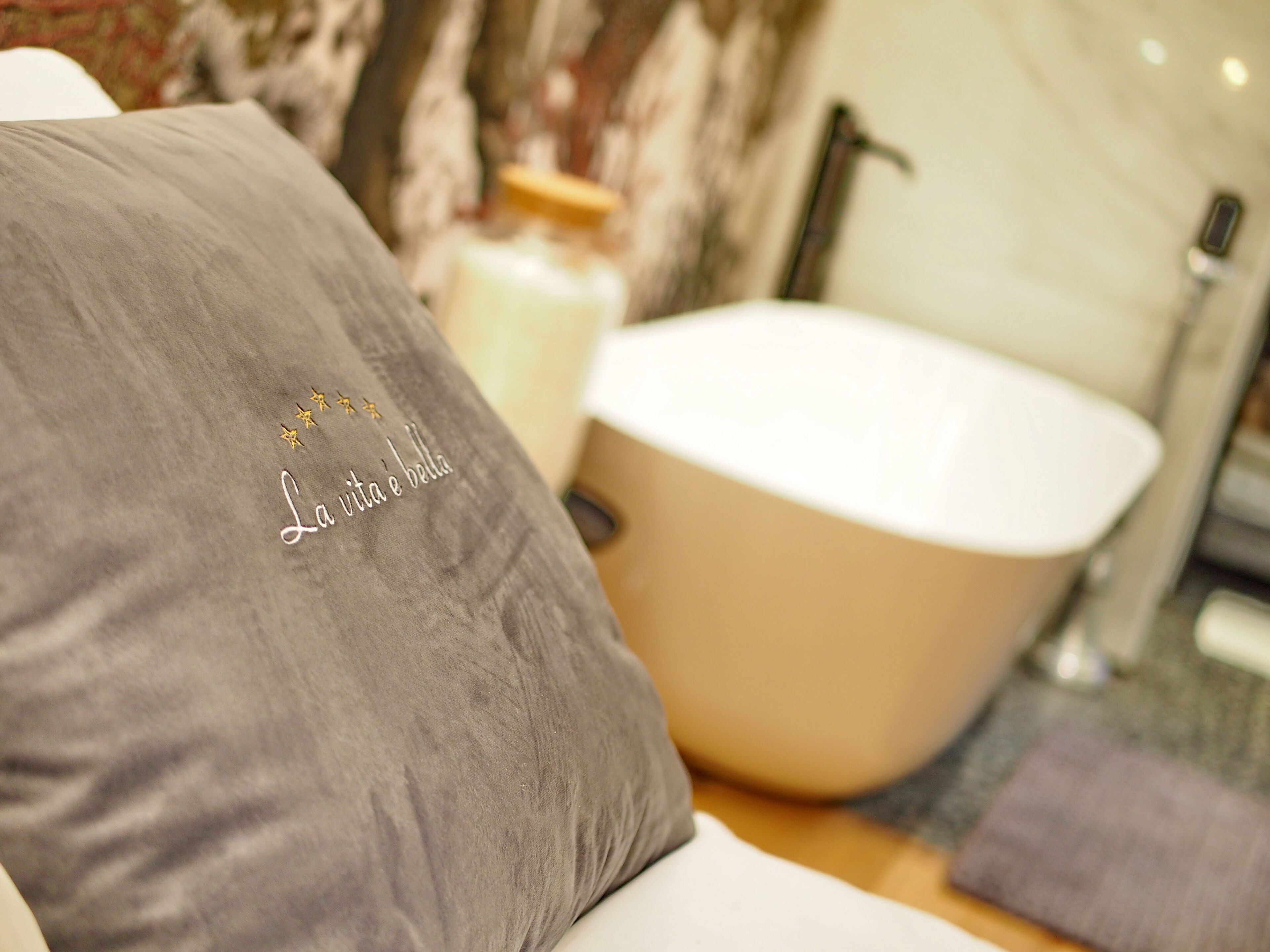 Un baño con bañera, una almohada gris con texto bordado y una botella de loción en el mostrador.