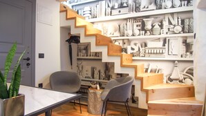 Un interior moderno con una escalera que sube a una zona superior, una mesa de comedor con sillas y una planta en maceta.