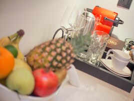 Uma bandeja de café da manhã com frutas, um copo, uma xícara branca e uma máquina de café.