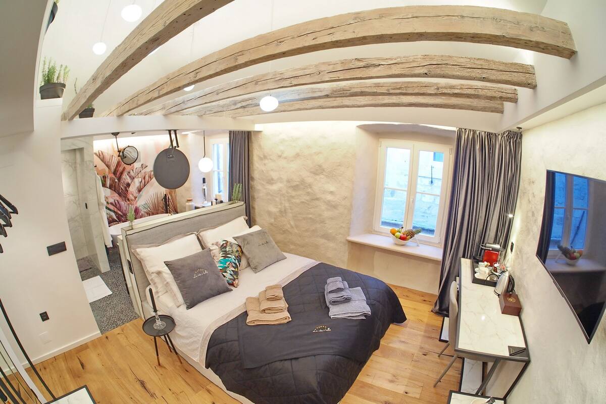 Une chambre moderne avec un grand lit, une petite table et une fenêtre avec des rideaux.