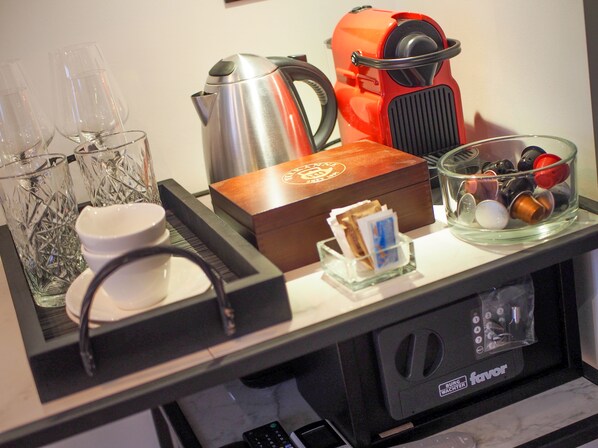 Una encimera de cocina con una cafetera, un hervidor, un recipiente de vidrio con cápsulas de café y una caja de vainas de café.