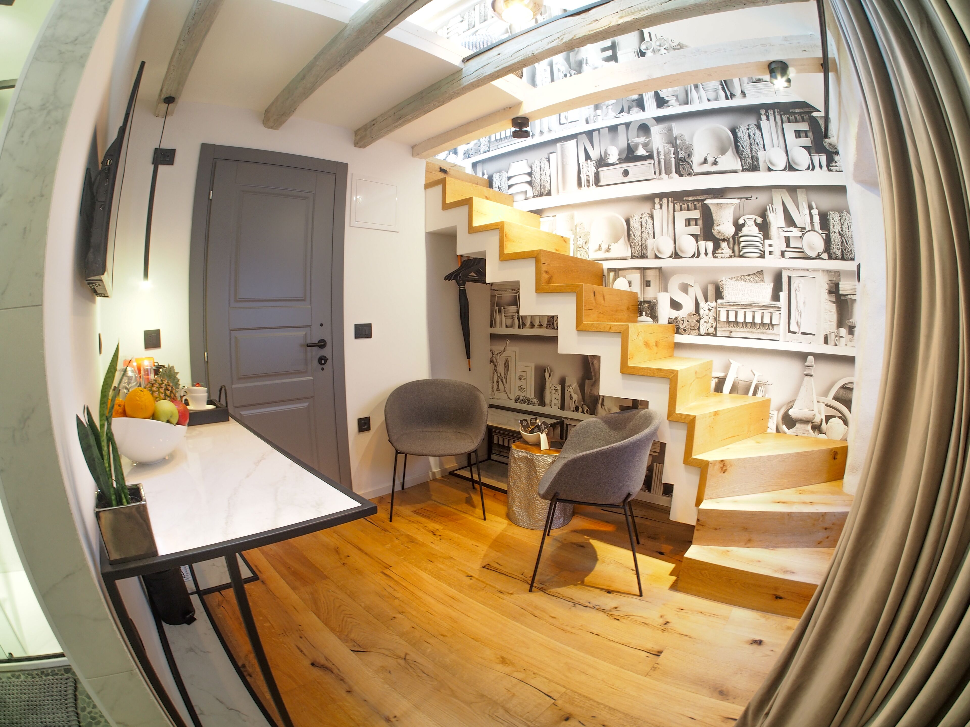 Un intérieur moderne avec un escalier en bois, un coin repas comprenant une table et des chaises, et un mur orné d’objets décoratifs.