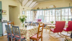 A dining area with a table set for four, surrounded by wooden chairs with floral upholstery. - 3 bedroom cottage, with far reaching views of the garden and open countryside. (Whitehills)