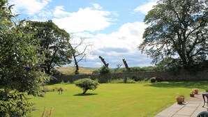 A well-maintained garden with a lawn, a small tree, and a stone wall. There are potted plants and a table with chairs. - 3 bedroom cottage, with far reaching views of the garden and open countryside. (Whitehills)