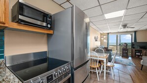A kitchen with a microwave, stove, and refrigerator. There is a dining area with a table and chairs. The room has a view of the ocean through large windows. - Oceanfront condos with 3 night minimum rentals and linens included! (Ocean City)