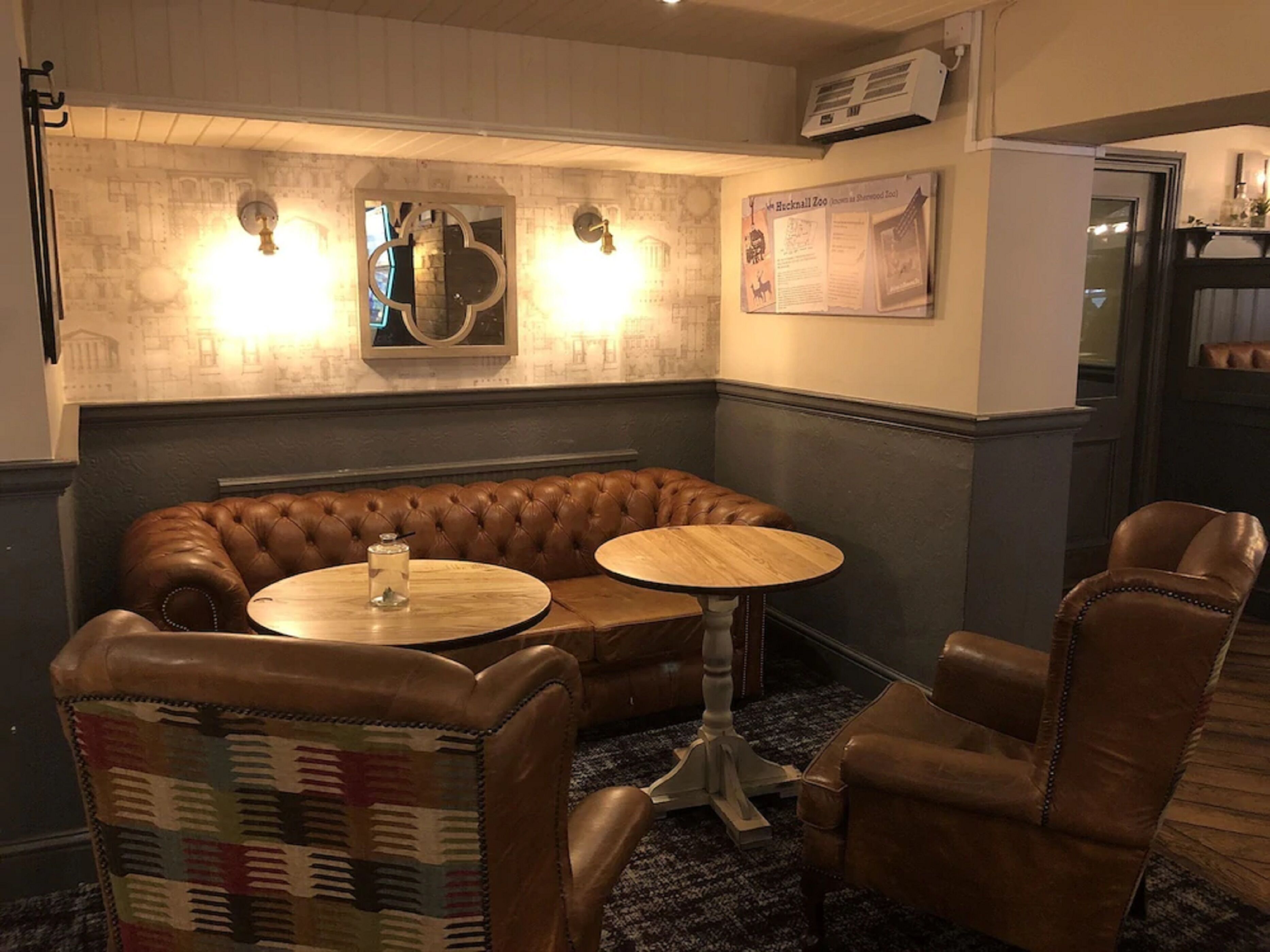 A cozy seating area with a brown leather sofa, two round wooden tables, and leather armchairs.