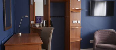 Habitación de hotel con un escritorio de madera, una silla, un armario, un televisor y un cartel que indica limpieza.