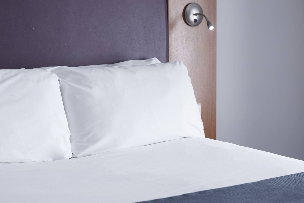 A neatly made bed with white linens and a dark headboard.