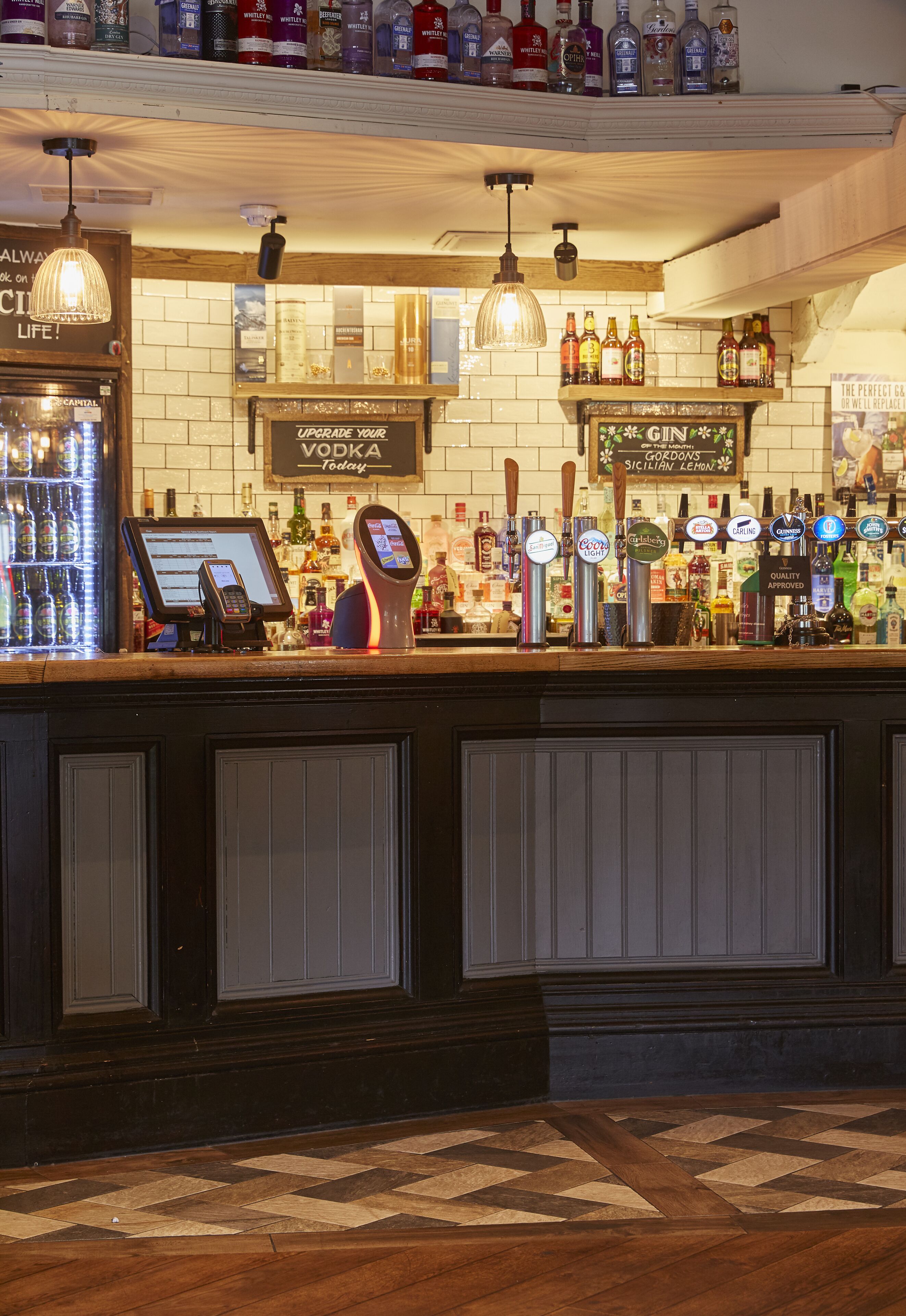 A bar area with a variety of liquor bottles, a cash register, and a wine cooler.