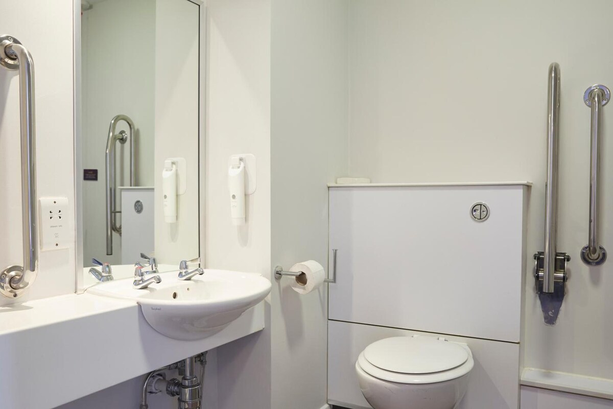 A bathroom with a white sink, mirror, toilet, and grab bars.