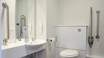 Un baño moderno con lavamanos, espejo y retrete blancos. Hay barras de apoyo en las paredes.
