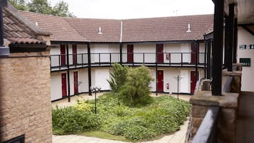 A courtyard with a central garden, a building with a tiled roof, and a fire exit sign.