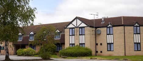 A row of brick buildings with dormer windows and a satellite dish, surrounded by greenery.