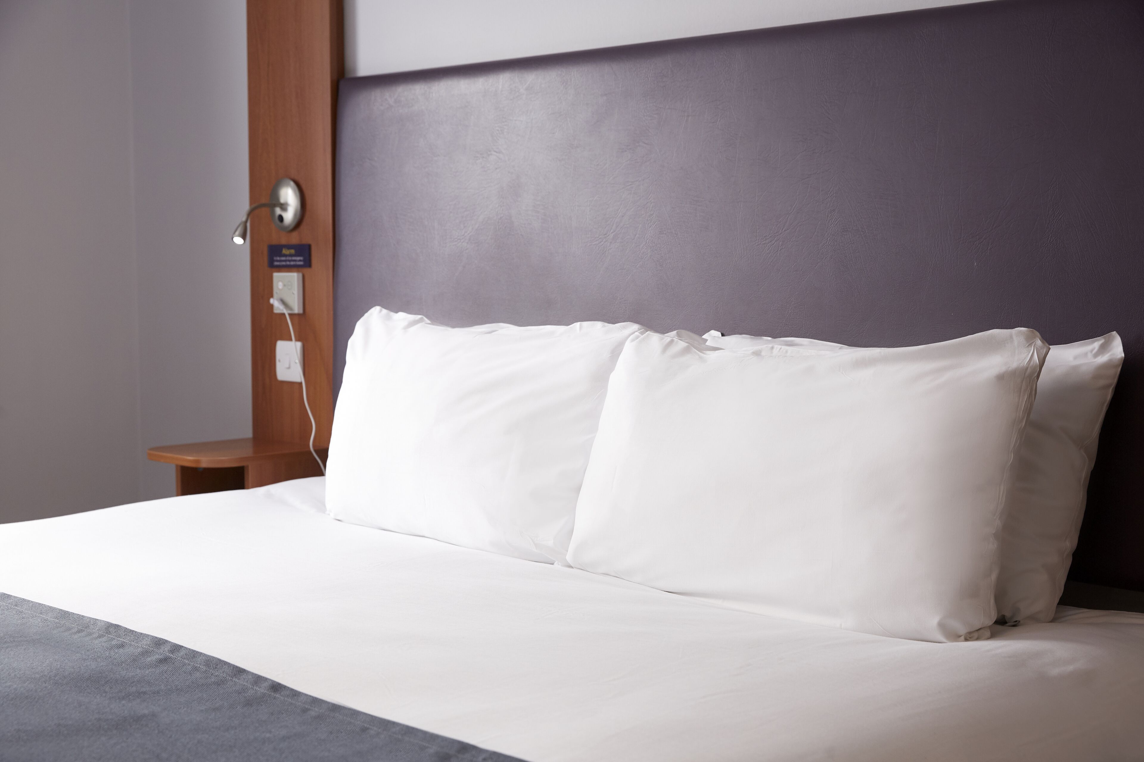 A neatly made bed with white linens and a grey accent at the foot.