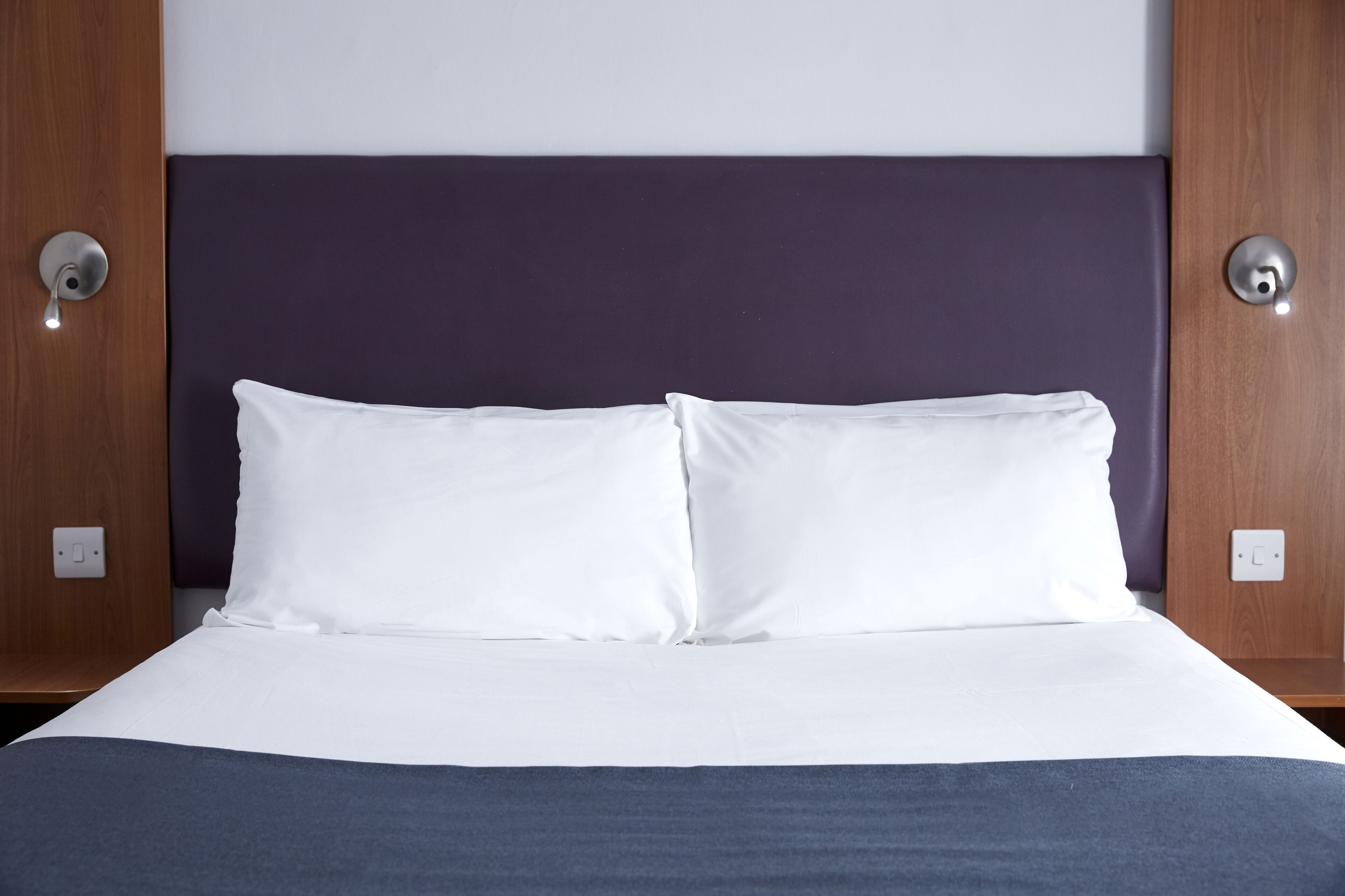 A neatly made bed with white linens and a dark headboard.