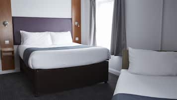 Habitación de hotel con una cama grande, una cama más pequeña, un cabecero de madera, una mesita de noche y una ventana con cortinas.