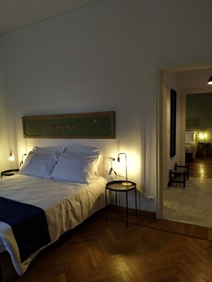 Une chambre d’hôtel comprenant un lit, des tables de chevet, une œuvre d’art accrochée au mur et un couloir menant à une autre pièce.