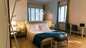 A hotel room with a bed, bedside table, lamp, chair, and a desk with a computer. - Palazzo Pasta Malpensa (Gallarate)