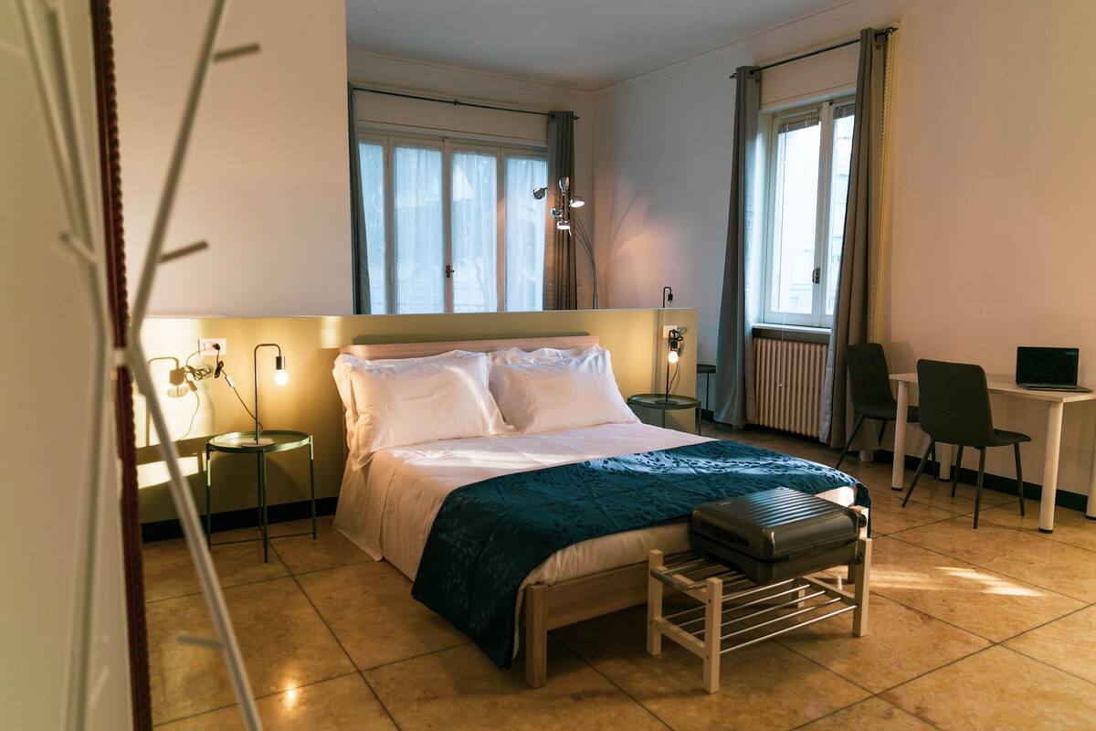 Une chambre d’hôtel comprenant un lit, une table de chevet, une lampe, une chaise et un bureau avec un ordinateur.