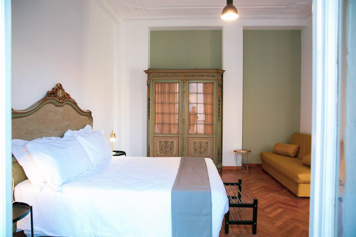 Une chambre avec un grand lit, une armoire verte, une petite table et un canapé.