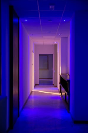 A hallway with a blue-lit ceiling and a wooden floor. - Palazzo Pasta Malpensa (Gallarate)