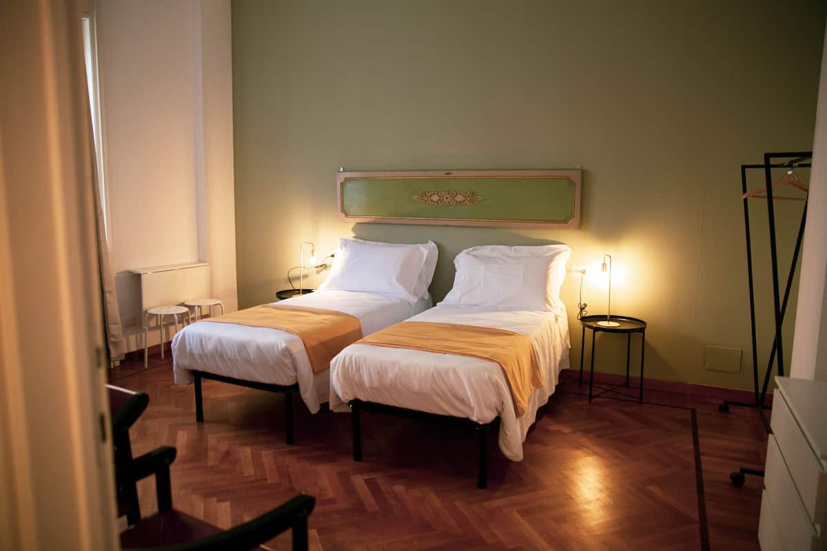 Une chambre avec deux lits, une petite table, une chaise, un radiateur et un miroir au mur.
