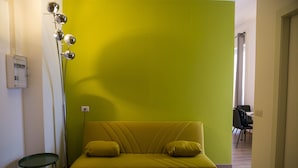 A yellow sofa with two cushions in a room with a green accent wall. - Palazzo Pasta Malpensa (Gallarate)