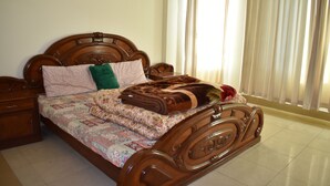 Una cama de madera con colcha y almohadas, una mesita de noche y una ventana con cortinas.