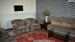 Una sala de estar con dos sillones, un sofá, un tapete estampado y un televisor instalado en la pared.
