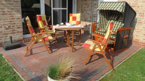 Eine Terrasse mit vier Holzstühlen und einem Tisch, einem kleinen Blumentopf und einer Backsteinmauer.
