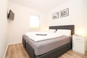 A neatly made bed with a grey headboard, a bedside table with a lamp, and two framed pictures on the wall.