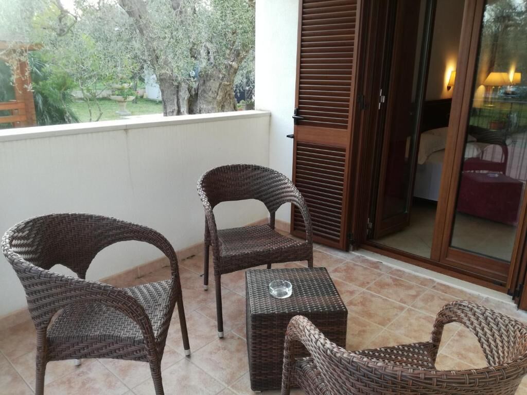 A balcony with wicker furniture, a glass table, and a view of greenery.