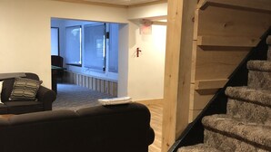 Ein Zimmer mit einer Holztreppe, einem schwarzen Sofa und Blick auf einen Balkon.